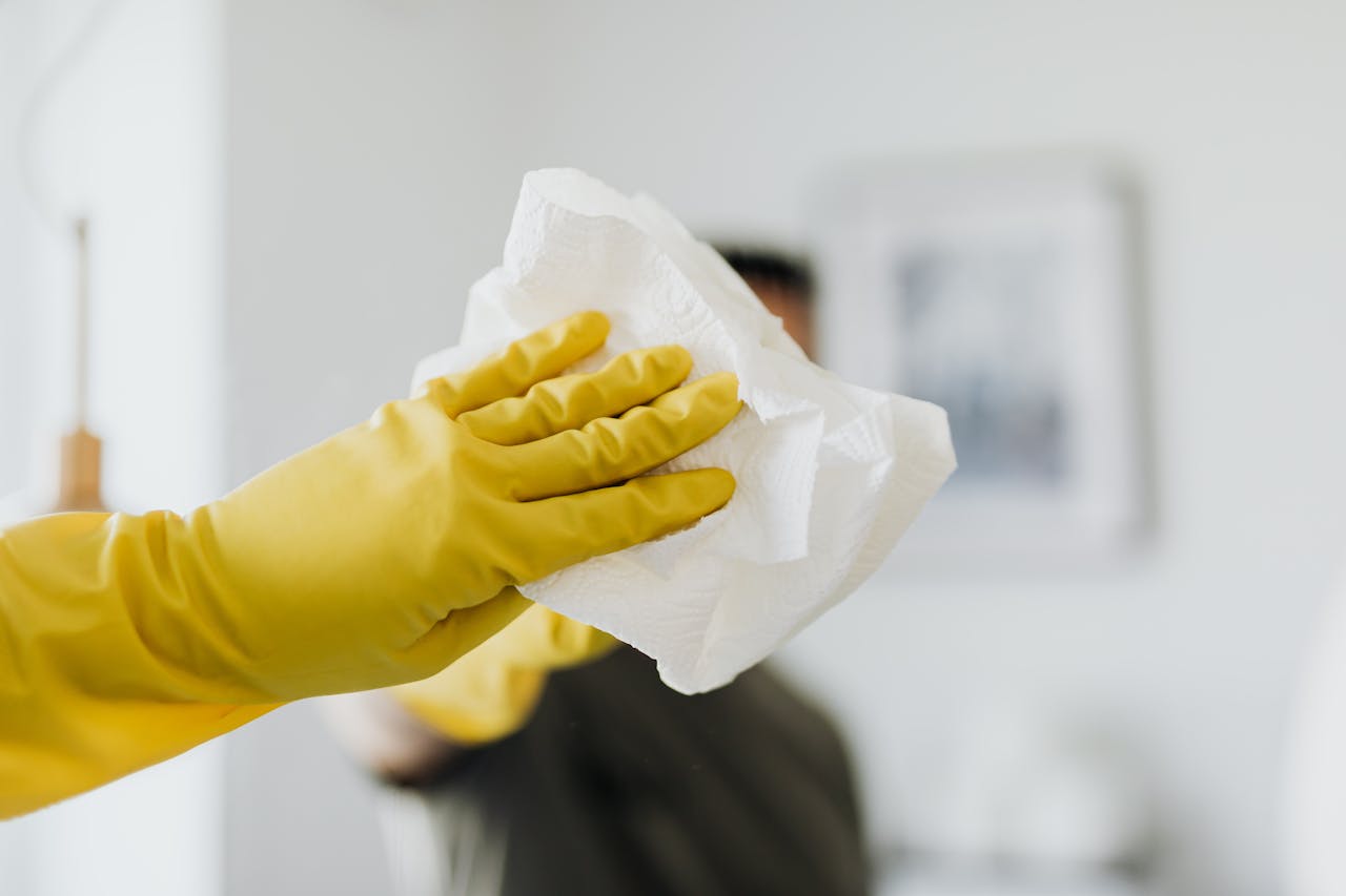 about-us-01 Close-up of a yellow-gloved hand cleaning a mirror with a cloth indoors.